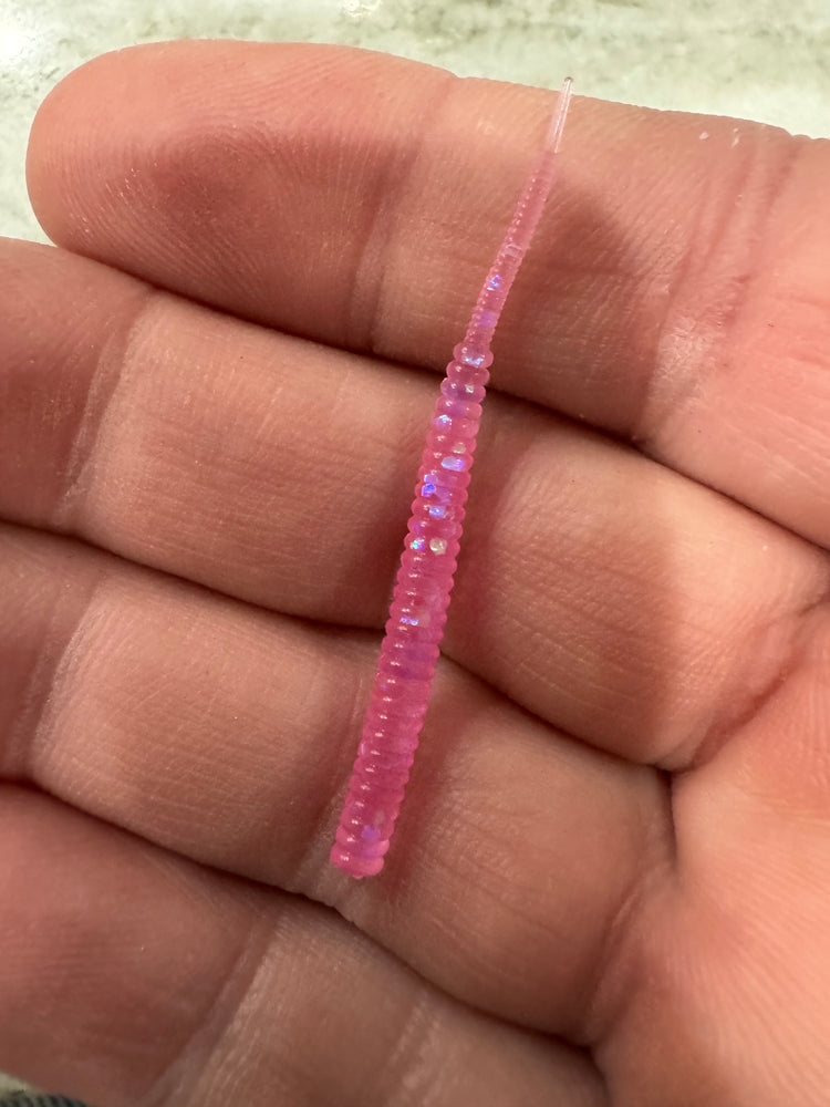 A hand holding a bright florescent pink 2” thin straight soft plastic worm with tiny silver glitter flakes