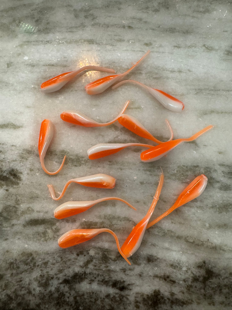 Multiple minnow shaped soft plastic Crappie Jigs, with a shiny orange back and a shimmering white under belly