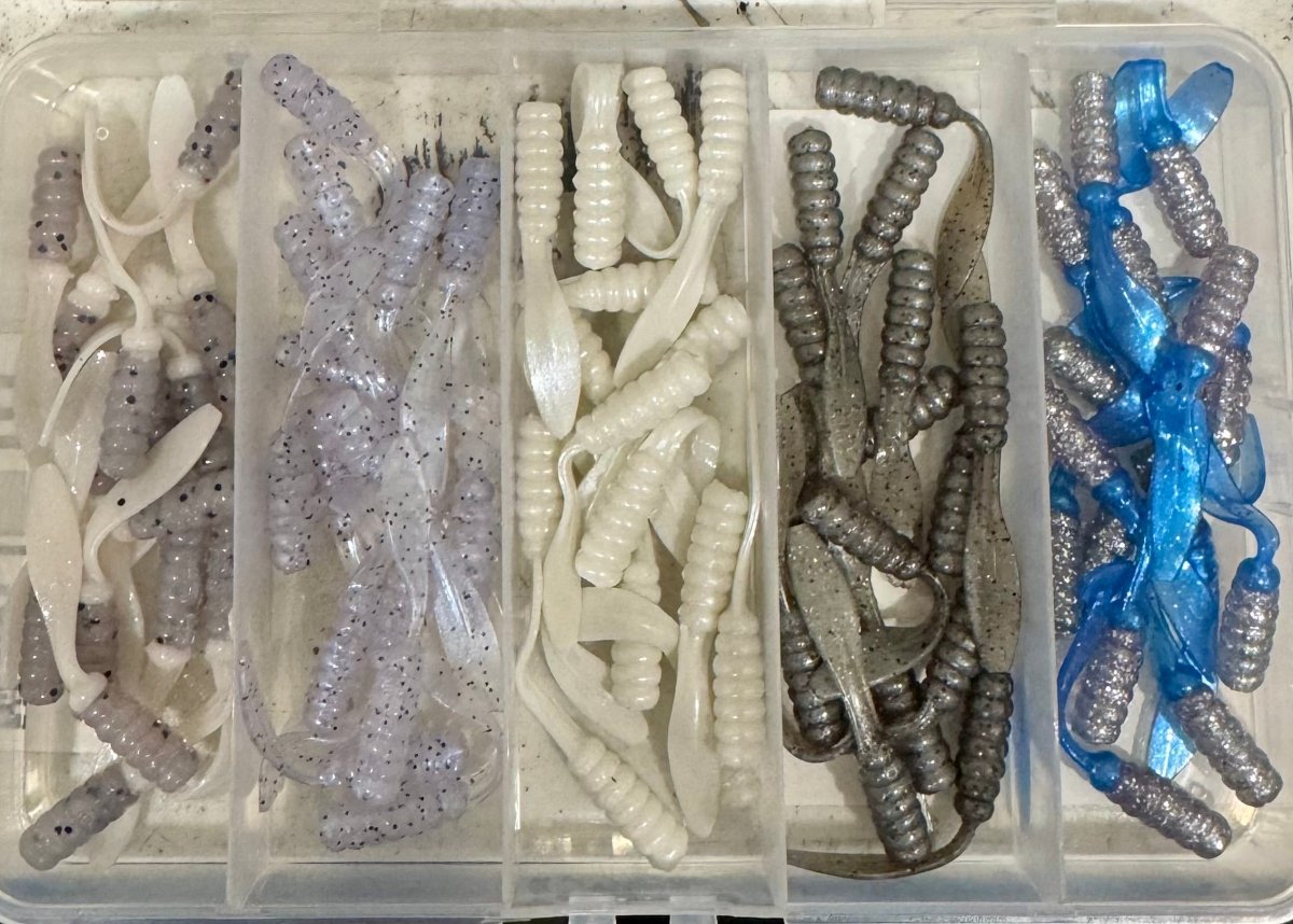 Open plastic box with different colors of crappie jigs. Clear/white, clear blue hue, white, grayish silver, blue/silver jigs.