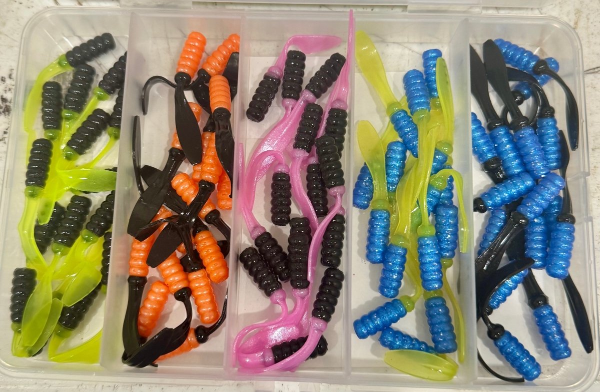 Small plastic box opened with different colors of crappie jigs in greens, orange, pink, black, and blue colors.
