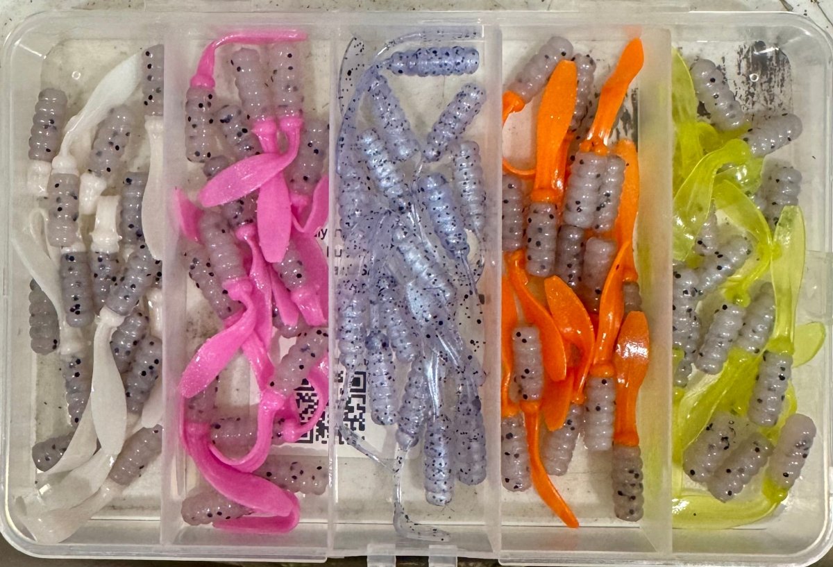 Open plastic box with different colors of crappie jigs. Clear/ white, clear/pink, clear blue hue, clear/orange, clear/green.