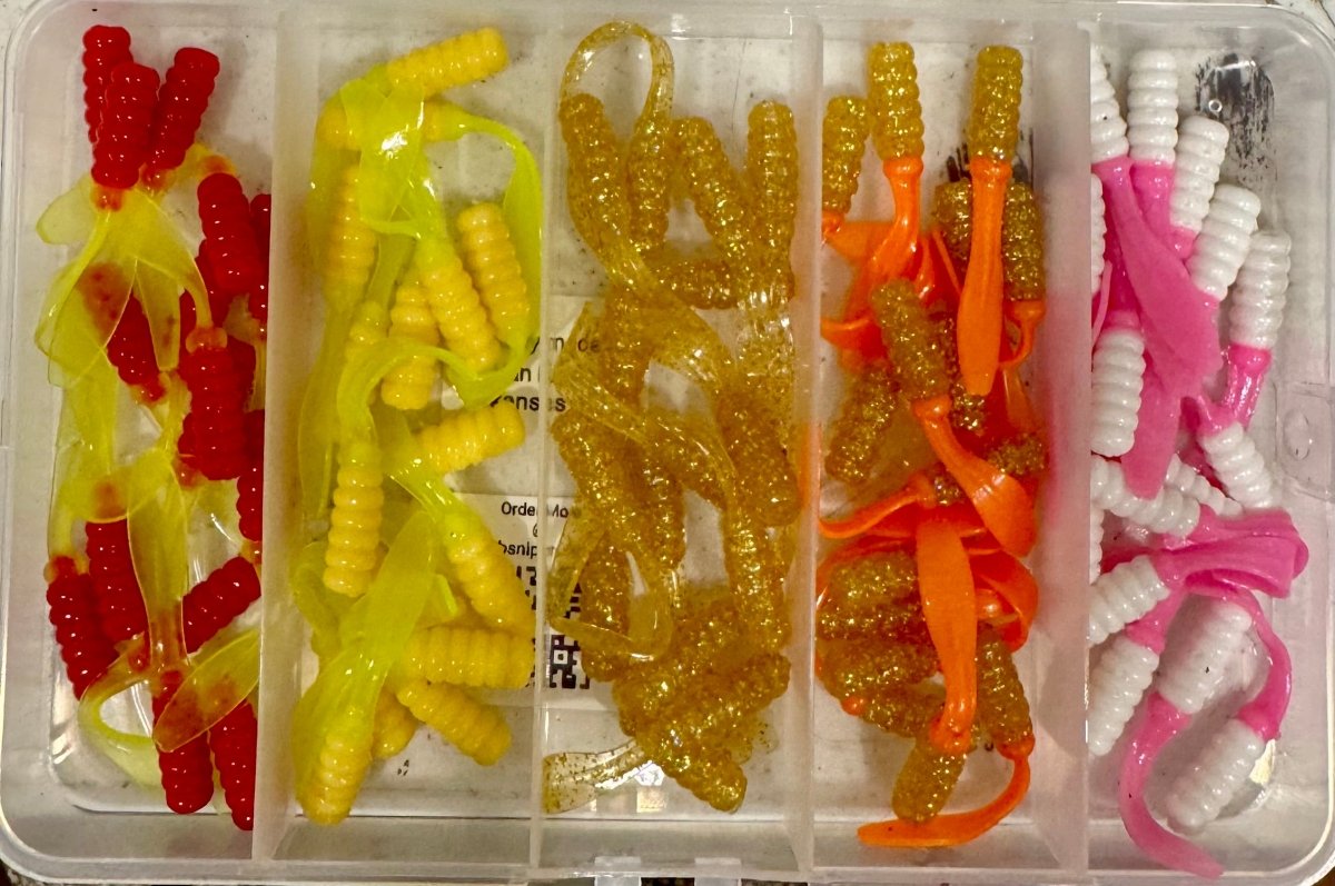 Open plastic box with different colors of crappie jigs. Red/Green, cream white/green, Gold, orange/gold, and pink/white jigs.