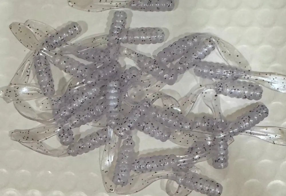 Soft plastic Crappie jigs with a translucent clear body with a faint blue hue and black glitter and a flat beaver tail